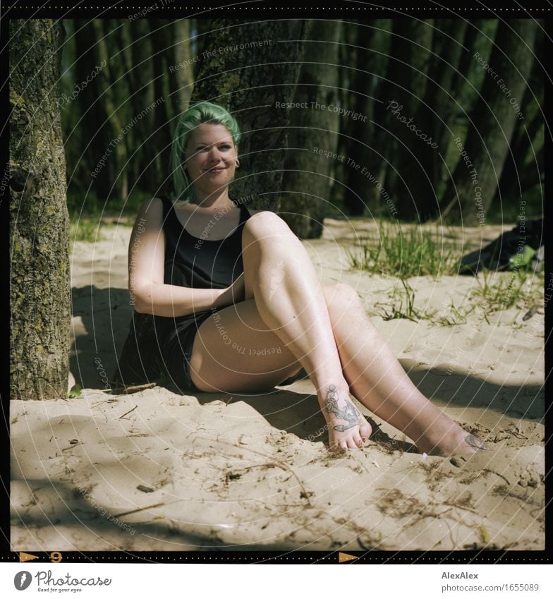 junge Frau sitzt in einem Wald am Strand mit übergeschlagenen Beinen und türkisem Haar und lächelt Freude Ausflug Sommer Junge Frau Jugendliche Fuß 18-30 Jahre