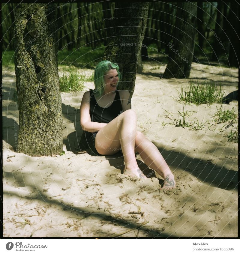 Junge Frau mit türkisen Haaren sitzt barfuß in einem Wald am Strand und lacht laut Leben Ausflug Sommerurlaub Jugendliche Körper Beine 18-30 Jahre Erwachsene