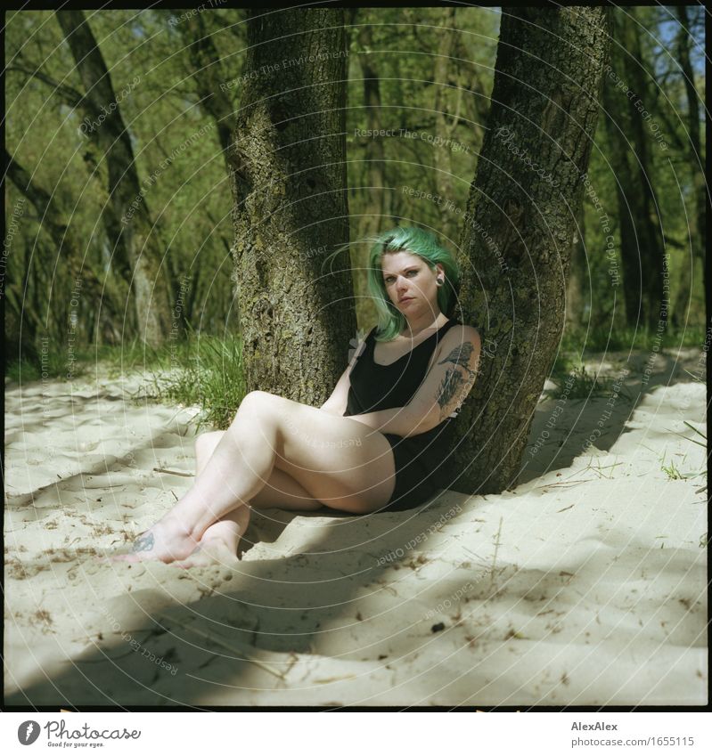Junge Frau mit türkisen Haaren sitzt barfuß im Strand- Wald an einen Baum gelehnt und schaut skeptisch in die Kamera ruhig Ausflug Sommerurlaub Jugendliche