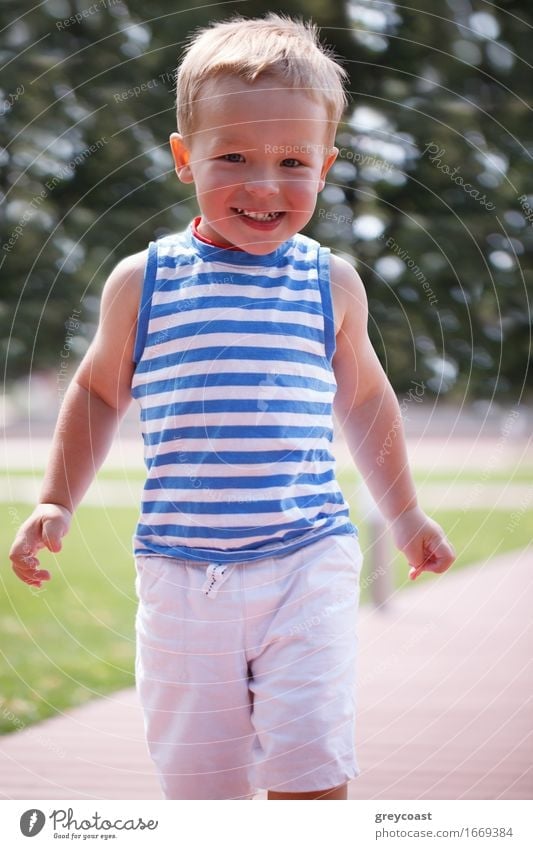 Porträt eines lächelnden glücklichen 3-jährigen Jungen in gestreifter Weste, der im Stadtpark läuft und zum Fotografen schaut Lifestyle Freude Glück schön