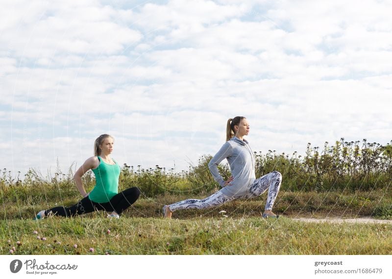 Zwei attraktive, athletische junge Mädchen, die draußen auf dem Lande Dehnübungen machen, um fit zu bleiben und ihre Muskeln zu straffen Lifestyle Freude schön