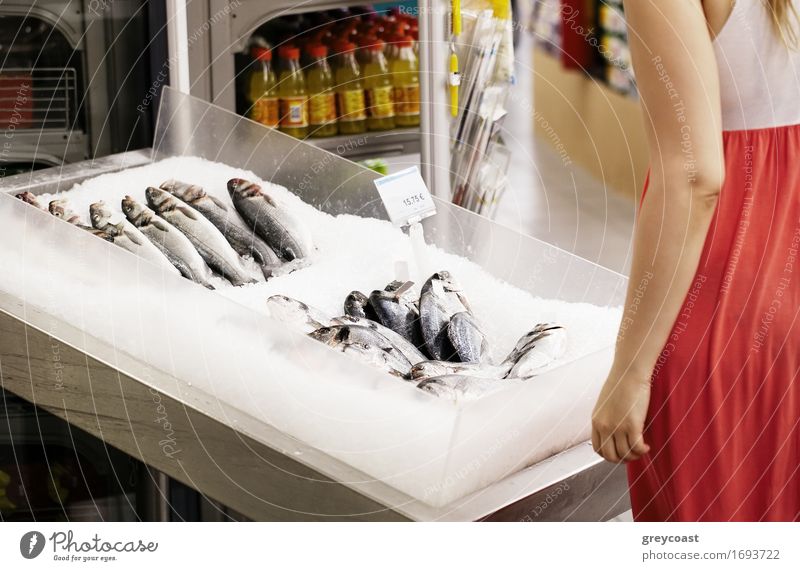Frau Einkaufen für Fisch in einem Supermarkt stehend Blick auf eine Anzeige von frischen ganzen Fisch auf Eis Lifestyle Glück Mensch Junge Frau Jugendliche