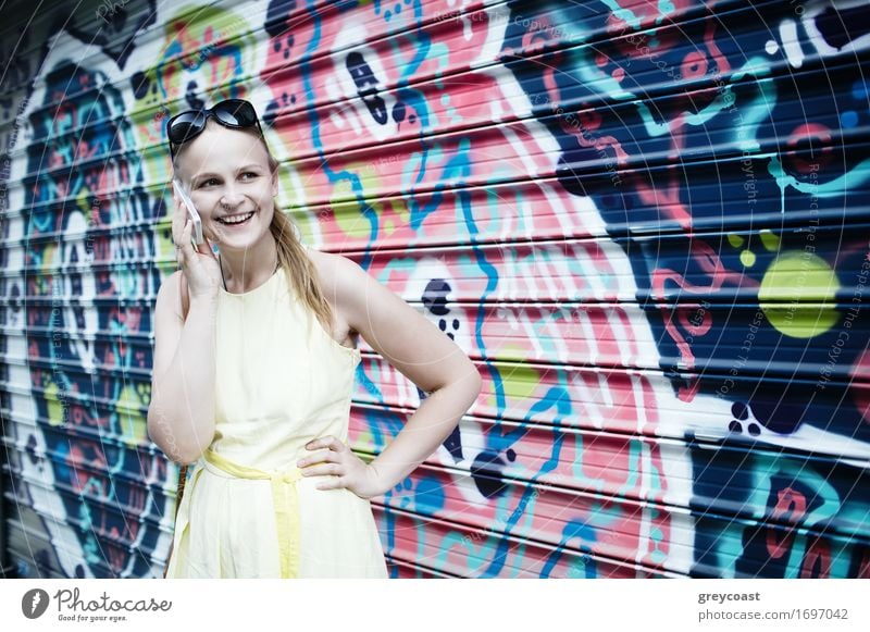 Lächelnde Frau im gelben Kleid steht und plaudert auf ihrem Smartphone vor einem auf Wellblech gemalten Graffiti Lifestyle Stil Glück schön Sommer