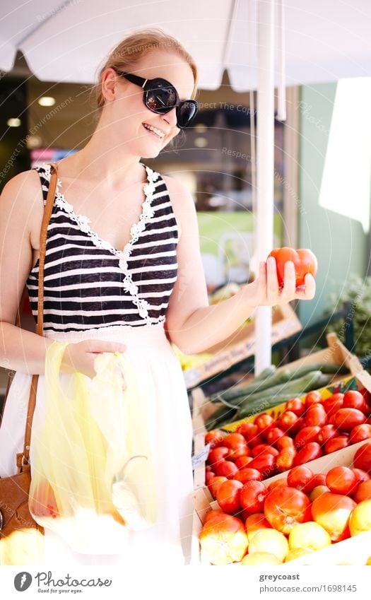 Junge Frau kauft frische Tomaten an einem Stand im Freien ein und wählt aus einer Reihe von Holzkisten aus Gemüse Frucht Apfel Korn kaufen Jugendliche