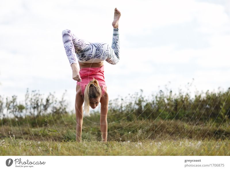Agile junge Frau macht einen Handstand im Freien in der Landschaft balancieren auf ihren Händen mit ihren Beinen in entgegengesetzte Richtungen gebogen Sport