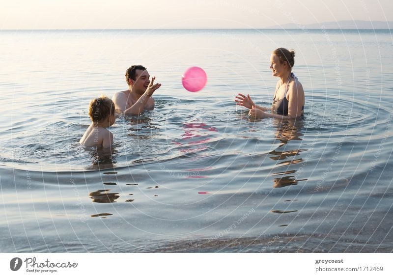 Junge Familie genießt das Meer bei Sonnenuntergang paddeln in den Untiefen zusammen spielen mit dem Ball, wie sie ihren Sommerurlaub genießen Freude Glück
