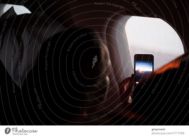 Frau, die während eines Fluges in einem Flugzeug mit ihrem Mobiltelefon durch ein Bullauge in der Kabine fotografiert Ausflug Telefon PDA Bildschirm Fotokamera