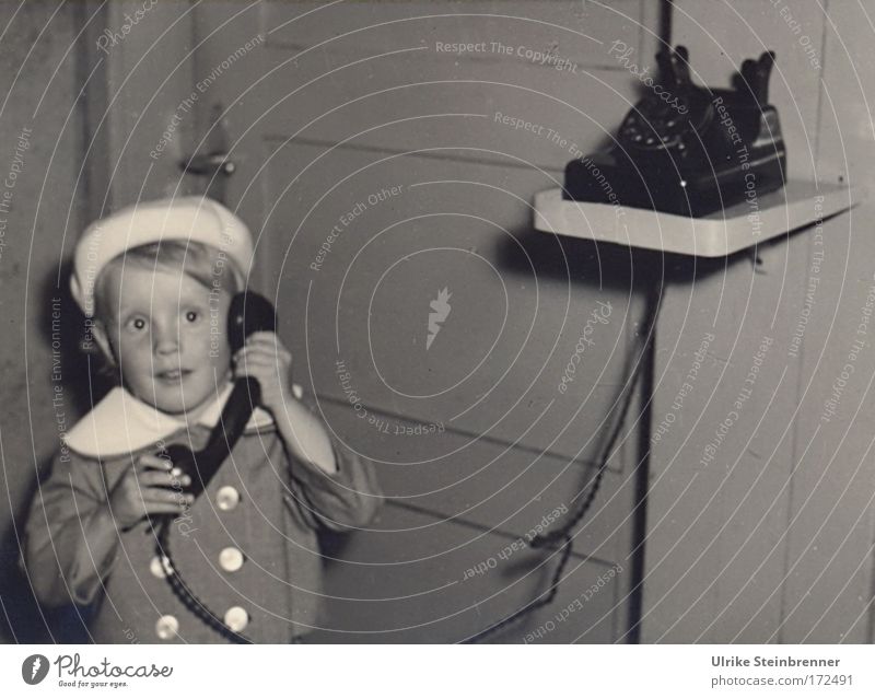 Kleines Mädchen mit Baskenmütze telefoniert Schwarzweißfoto Innenaufnahme Textfreiraum rechts Blitzlichtaufnahme Oberkörper Vorderansicht Blick nach vorn