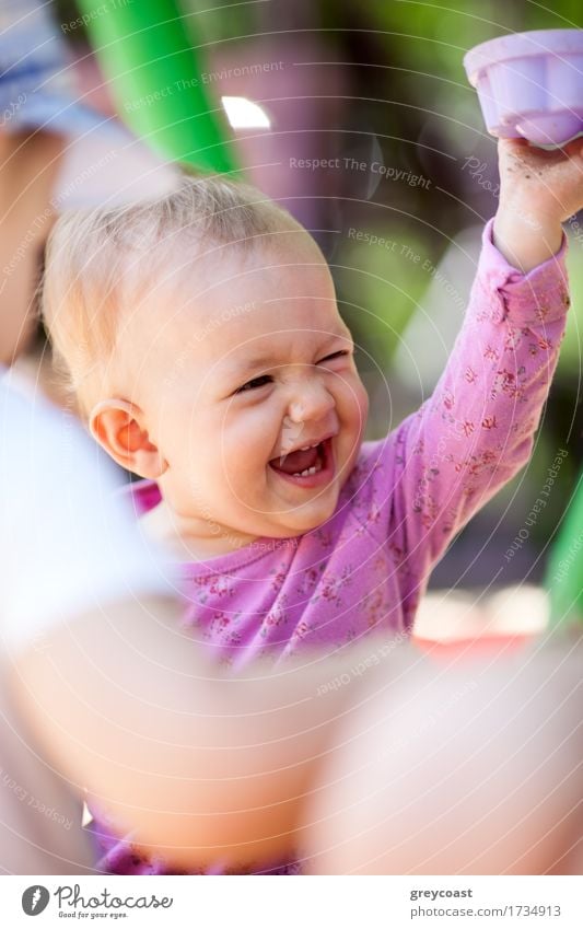 Adorable glücklich lachend kleines Baby spielt mit einem Spielzeug, wie es auf seine Mütter Schoß sitzt, offenes Porträt über die Schulter der Mütter Freude
