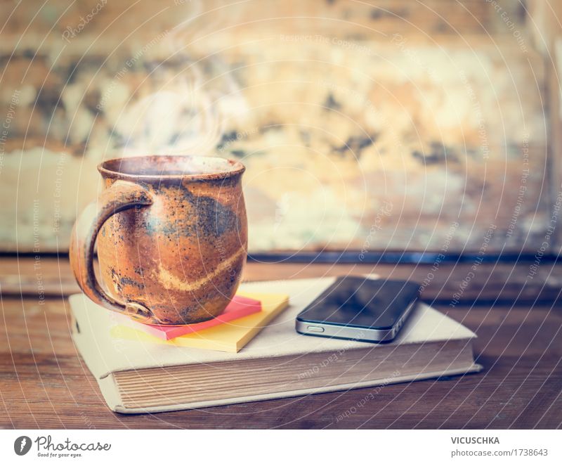 Tasse mit heißem Getränk auf Buch mit Smart-Phone Heißgetränk Kaffee Tee Lifestyle Stil Design Häusliches Leben Tisch Handy PDA retro altehrwürdig Wasserdampf
