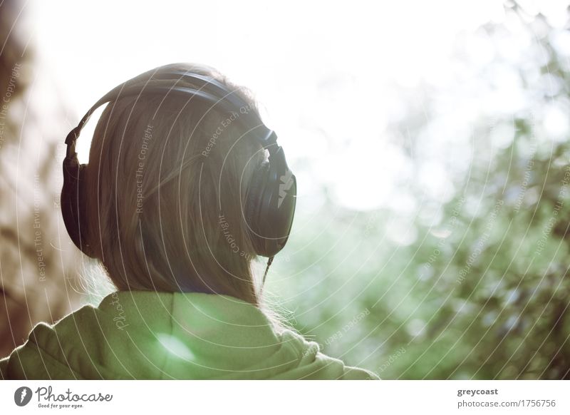 Vintage-Foto einer Frau mit Kopfhörern Musik hören im Freien gegen helles Sonnenlicht. Instagram-Stil Farbe getönt Erholung Freizeit & Hobby Garten