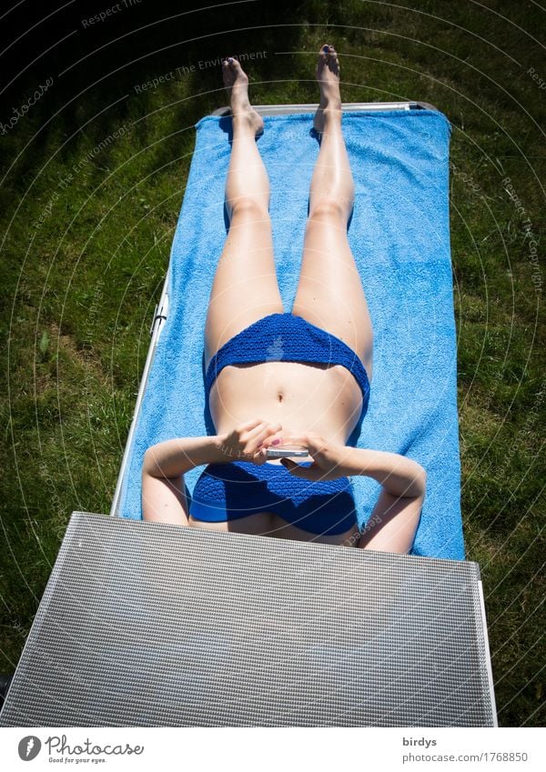 Junge Frau sonnt sich im Bikini auf einer Liege und spielt mit dem Smartphone Jugendliche Körper Erholung schlank Sonnenbad Badetuch Liegestuhl feminin chillen