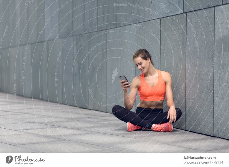 Sportliche junge Frau, die auf Vorhof mit ihrem Mobile sitzt Glück lesen PDA feminin Erwachsene 1 Mensch 18-30 Jahre Jugendliche Strumpfhose Lächeln sitzen