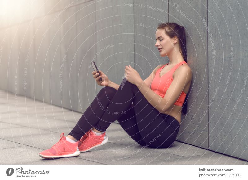 Sportliche junge Frau, die auf Vorhof mit ihrem Mobile sitzt Glück lesen PDA feminin Erwachsene 1 Mensch 18-30 Jahre Jugendliche Strumpfhose Lächeln sitzen