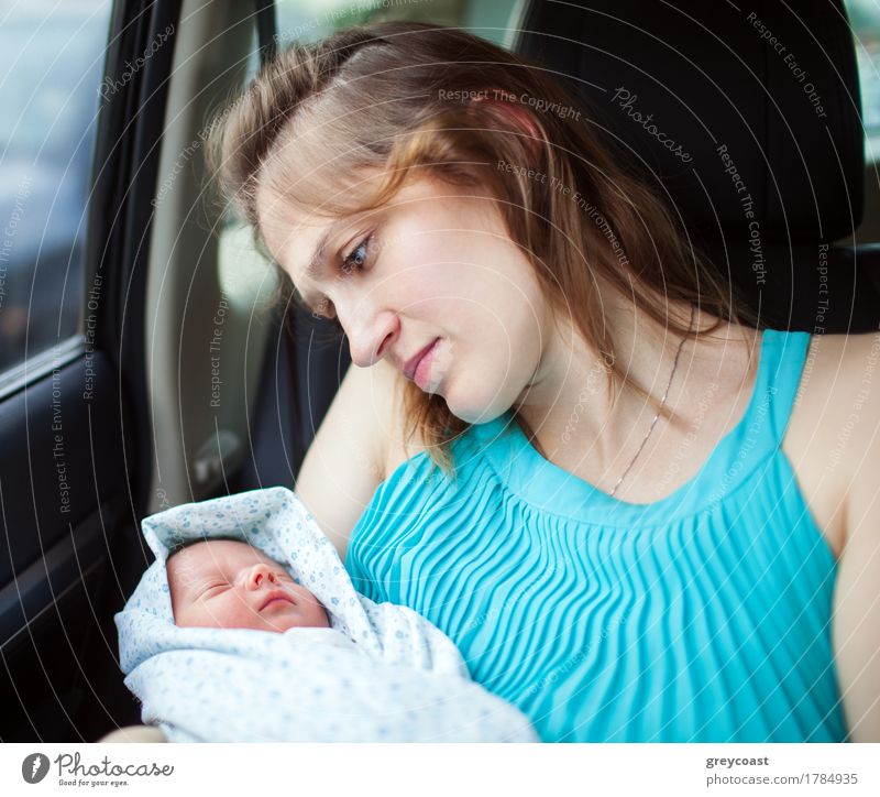 Junge Mutter hält Neugeborenes in Babydecke eingewickelt, während sie im Auto sitzt. Frau schaut auf ihr Baby mit tiefen Gefühlen in den Augen ausgedrückt Kind