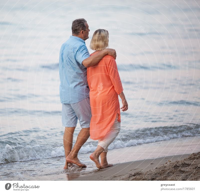 Senior Paar zu Fuß zusammen entlang der Küste. Mann umarmt die Frau, während sie genießen barfuß Ausflug am Strand haben Erholung Windstille