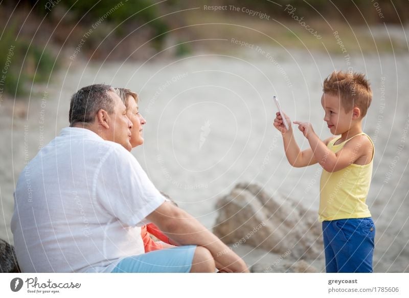 Lächelndes kleines Kind mit Smartphone, das ein Bild von glücklicher Großmutter und Großvater macht. Familie Freizeit im Freien Glück Sommer Strand Telefon PDA