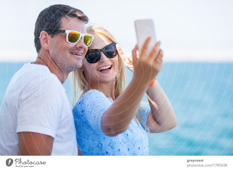 Glücklicher junger Mann und Frau mit modischer Sonnenbrille nehmen Handy-Selfie auf dem Hintergrund der defokussierten blauen Meer. Urlaub Fotos Stil