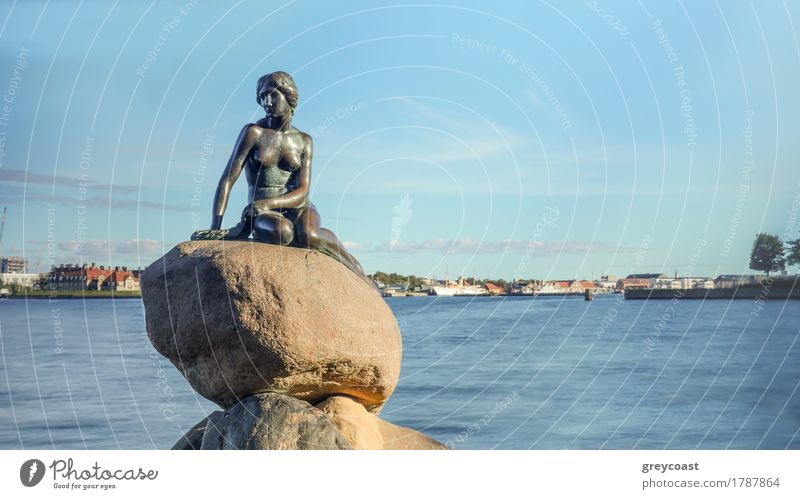 Frontansicht der kleinen Meerjungfrau Statue auf großen Felsbrocken in Dänemark mit Hafen unter blauem Himmel im Hintergrund Ferien & Urlaub & Reisen Tourismus