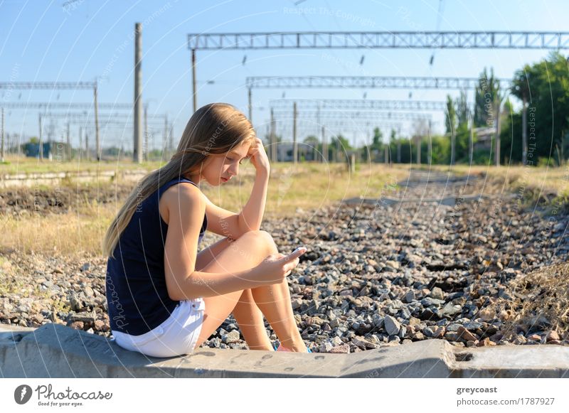 Mädchen Teenager in Top und Shorts mit Handy während des Sitzens auf Beton der unvollendeten Bahnstrecke auf dem Lande Sommer Telefon PDA Frau Erwachsene