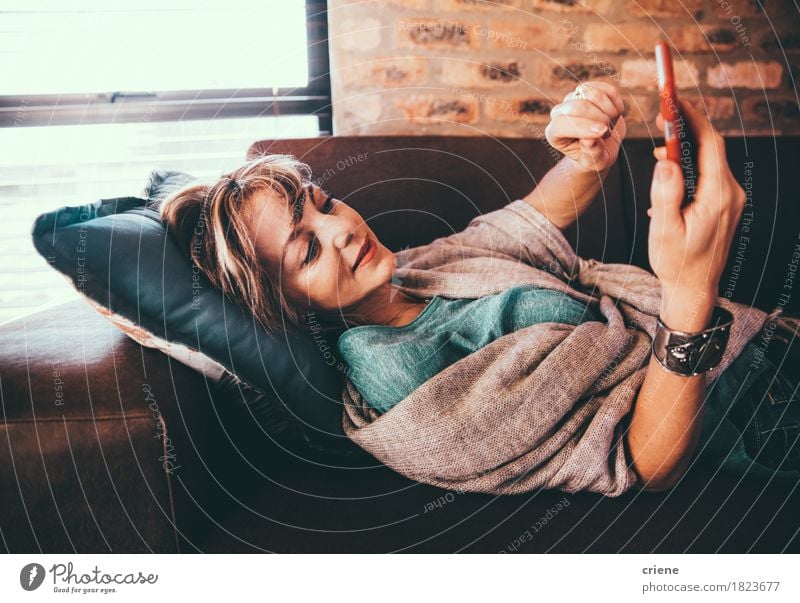 Moderne reife Frau, die auf Couchgraseninternet legt Erholung Wohnzimmer Handy PDA Internet Erwachsene modern bequem digital Touchscreen Browsen