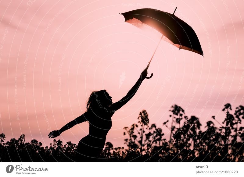 Abgekoppelte Frau in Silhouette mit Schirm fliegt in die Zukunft. Warme Szene mit fliegendem Mädchen. Zeigt die Vorstellungskraft und den Aufbruch zu neuen Horizonten wie Klimawechsel oder Achtsamkeit.
