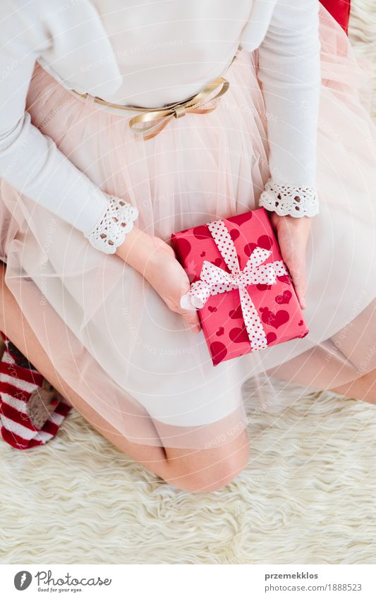 Mädchen, das Weihnachtsgeschenk hält und auf einem Teppich sitzt Lifestyle Feste & Feiern Weihnachten & Advent Kind Mensch 1 8-13 Jahre Kindheit Kleid rosa rot