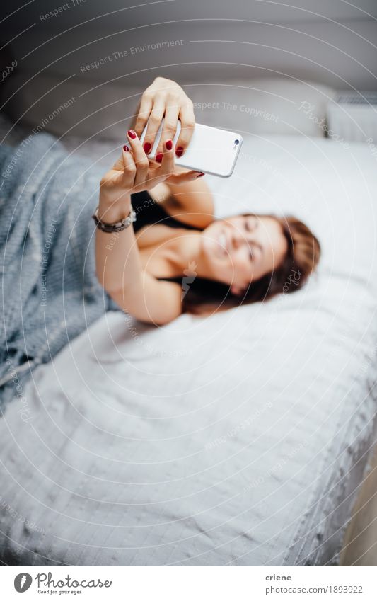 Das Legen der jungen Frauen entspannte sich auf dem Bett, das selfies nimmt Lifestyle Freude ruhig Häusliches Leben Haus Innenarchitektur Schlafzimmer Telefon