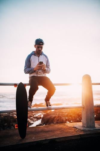 Junger erwachsener Mann, der auf dem Geländerbrowsen mit intelligentem Telefon sitzt Lifestyle sprechen Handy PDA Technik & Technologie Unterhaltungselektronik