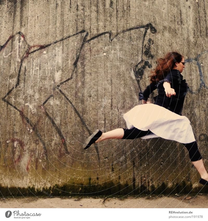 Frau springt vor einer Mauer Mensch feminin Junge Frau Jugendliche 1 18-30 Jahre Erwachsene Wand Rock Leggings langhaarig Bewegung laufen rennen springen trendy