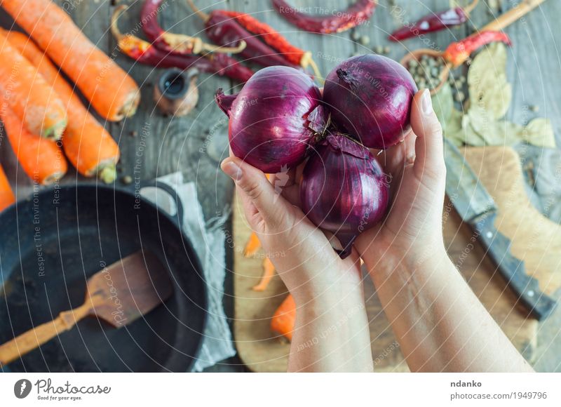 emale Hände halten drei rote Zwiebeln Lebensmittel Gemüse Kräuter & Gewürze Ernährung Vegetarische Ernährung Pfanne Messer Löffel Tisch Küche Junge Frau