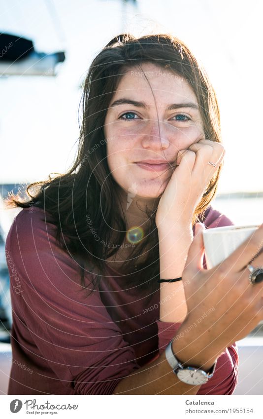 Eine junge Frau mit Kaffeetasse in der Hand schaut lächelnd in die Kamera trinken Segeln Sommer Meer Jachthafen beobachten genießen Duft schön blau braun rosa