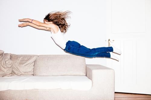 Langhaariges Mädchen in Jeans springt kopfüber in ein Sofa feminin Kind 8-13 Jahre Kindheit Jeanshose brünett langhaarig fliegen springen frech Fröhlichkeit