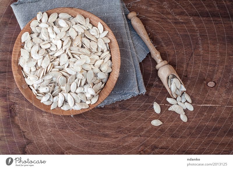 Ungeschälte Kürbiskerne in einer hölzernen Schüssel Gemüse Schalen & Schüsseln Löffel Tisch Küche Holz frisch oben braun grau weiß Samen Snack Feinschmecker Top