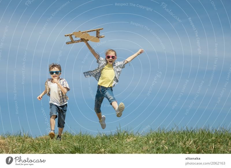Zwei kleine Kinder spielen tagsüber im Park mit einem Spielzeugflugzeug aus Pappe. Konzept des glücklichen Spiels. Kind hat Spaß im Freien. Bild vor dem Hintergrund des blauen Himmels.