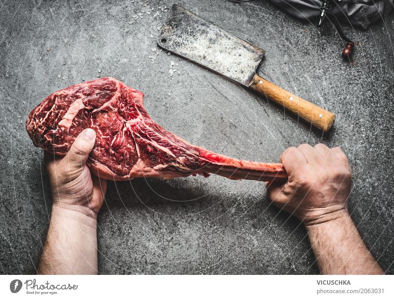 Tomahawk Rindersteak in männlichen Händen mit Fleisch Hacker Lebensmittel Stil Tisch Küche Restaurant maskulin Hand Grill Beton Design Steak Mann stoppen
