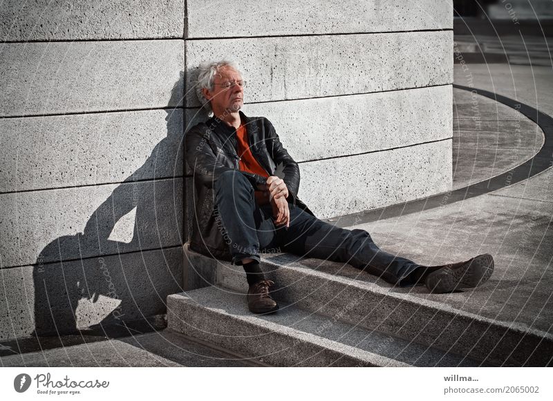 Ein Mann sonnt sich im Schatten seiner selbst Brille weißhaarig Locken sitzen ausruhen Pause Erholung Betonwand maskulin Mensch Erwachsene urban ausruhend