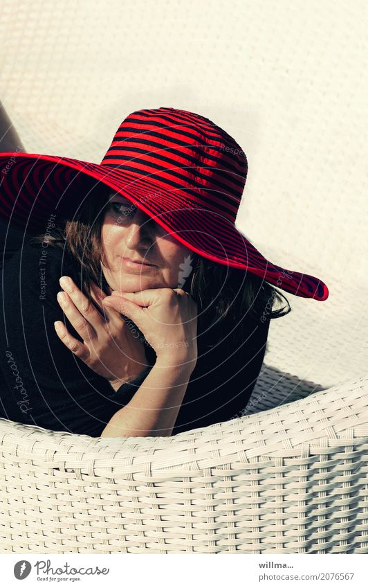 Lady mit rotem Hut liegt beobachtend auf weißer Korbliege in der Sonne Lifestyle elegant harmonisch Wohlgefühl Zufriedenheit Erholung Sommer Sommerurlaub