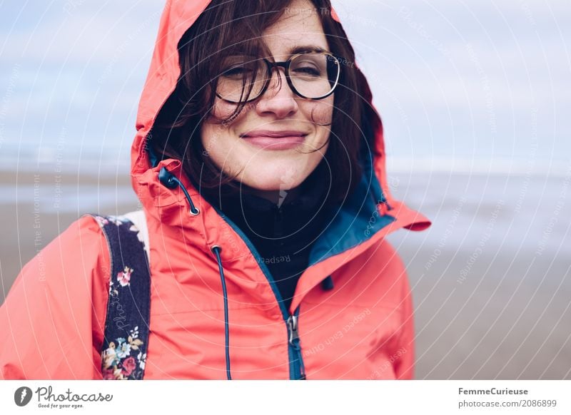 Junge Frau mit Brille und roter Regenjacke am Meer feminin Jugendliche Erwachsene 1 Mensch 18-30 Jahre 30-45 Jahre Natur Lächeln Glück Zufriedenheit