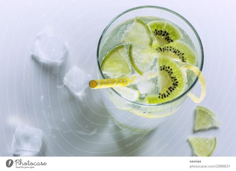 Kühles Erfrischungsgetränk mit Kiwi und Limette in einem Glas mit gelben Trinkhalm Getränk Limettenscheibe Zitronenschale Limone Trinkwasser Frucht Eiswürfel