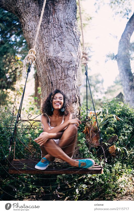 Glückliche afrikanische junge Frau, die auf Schwingen unter Baum im Garten sitzt Lifestyle Wohlgefühl Sommer Sonne Mensch feminin Junge Frau Jugendliche 1 Natur