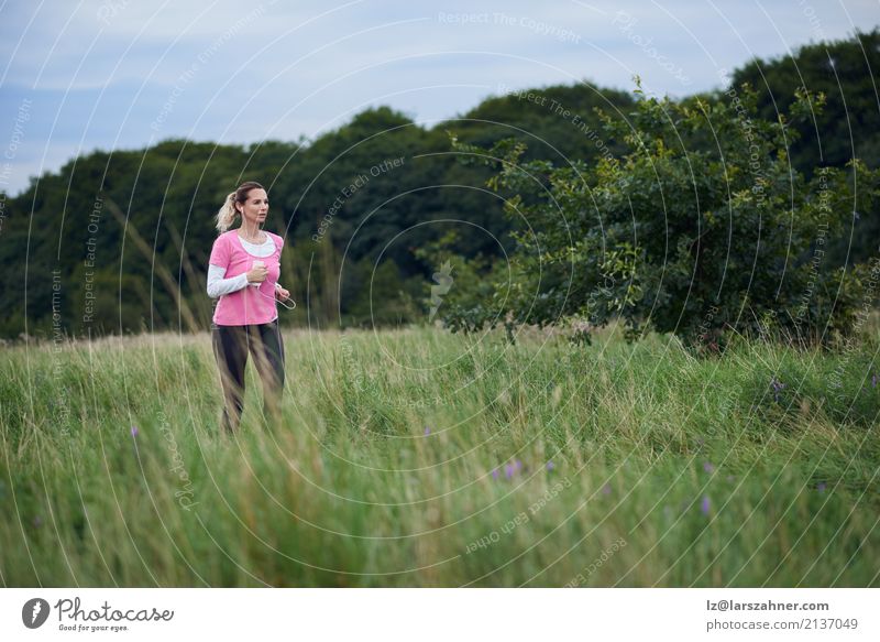 Geeignete Frau von mittlerem Alter, die durch ein Feld läuft Lifestyle Glück Sommer Sport Joggen Telefon Handy Erwachsene Natur Wege & Pfade blond Fitness