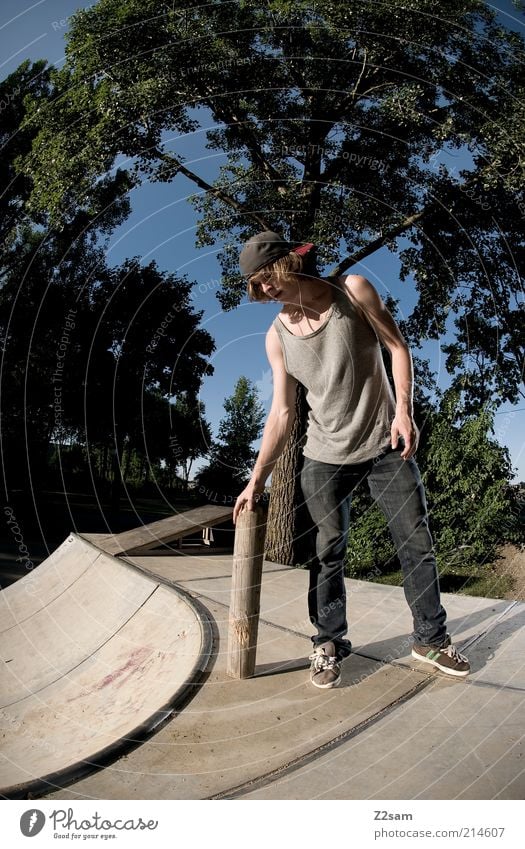 SKATER BEI DER ARBEIT Stil Skateboard Skateboarding maskulin Junger Mann Jugendliche Jugendkultur Baum Park T-Shirt Jeanshose Mütze berühren festhalten stehen