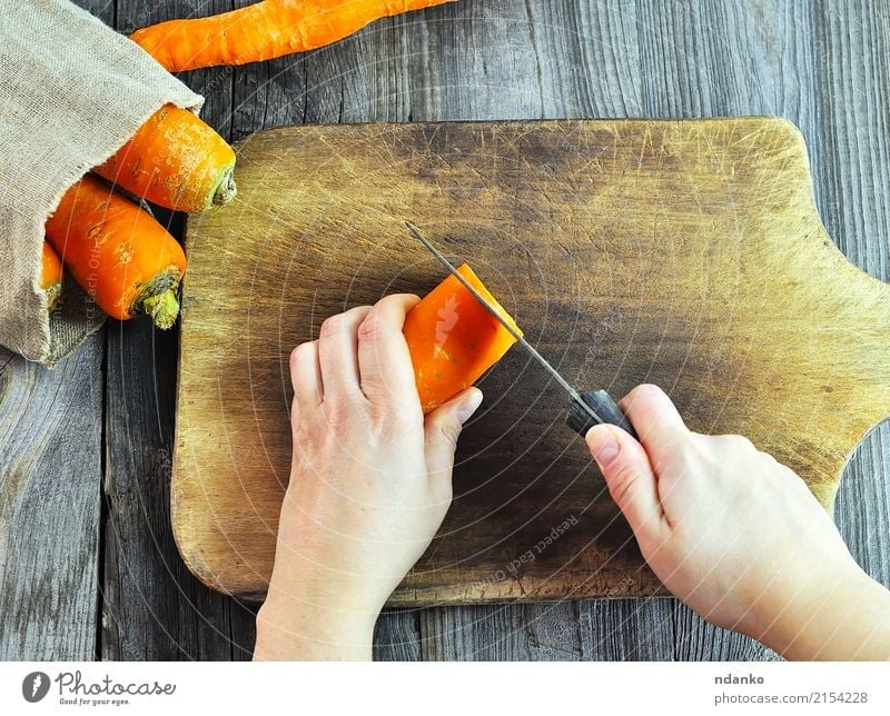 Zwei weibliche Hände mit einem Messer Lebensmittel Gemüse Essen Körper Küche Frau Erwachsene Hand frisch grau Möhre orange Scheitel Holzplatte Essen zubereiten