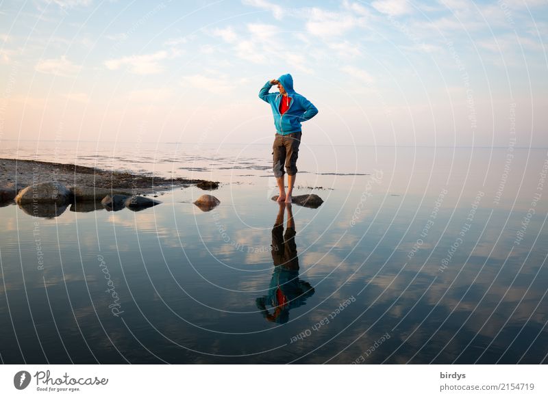 Mann mit blauer kapuzenjacke steht auf einem Stein im Wasser der ostsee und blickt Richtung Festland Küste Ostsee ruhig Erwachsene beobachten 1 Barfuß Mensch