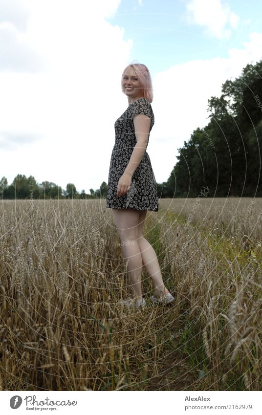 Portrait einer jungen Frau in einem Sommerkleid, die in einem Feld steht und sich lächelnd umdreht Getreide Freude schön Körper Zufriedenheit Ausflug Abenteuer