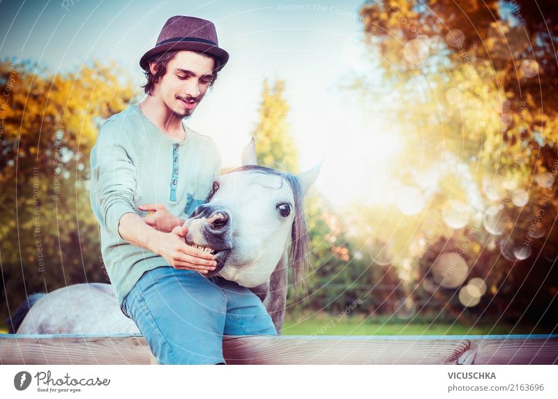 Junger Mann sitzt auf dem Zaun und füttert Pferd Lifestyle Stil Mensch Jugendliche 1 Natur Tier Gefühle Stimmung young Tierliebe Freundschaft Farbfoto