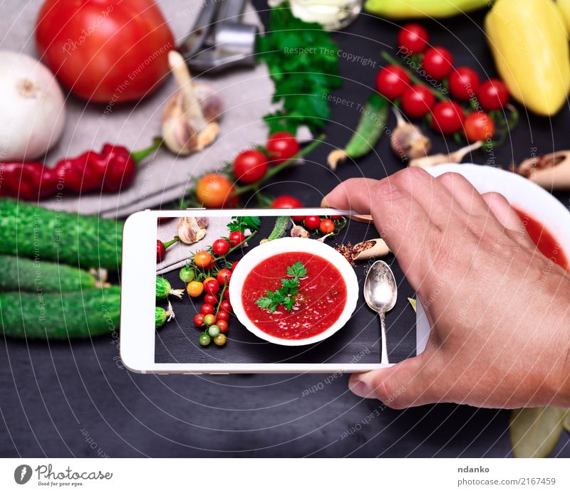 Smartphone in der menschlichen Hand Gemüse Suppe Eintopf Ernährung Mittagessen Abendessen Vegetarische Ernährung Diät Teller Löffel Tisch Küche PDA Holz frisch
