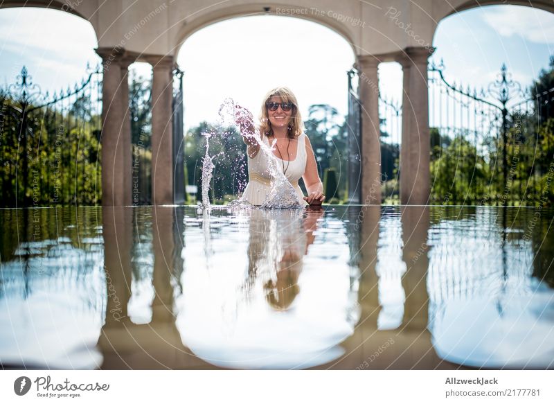 Frau mit Sonnenbrille spielt mit Wasser Tag Reflexion & Spiegelung Sommer Freude spaßig Haus feminin Junge Frau Brunnen Wasserbecken Gebäude blond langhaarig