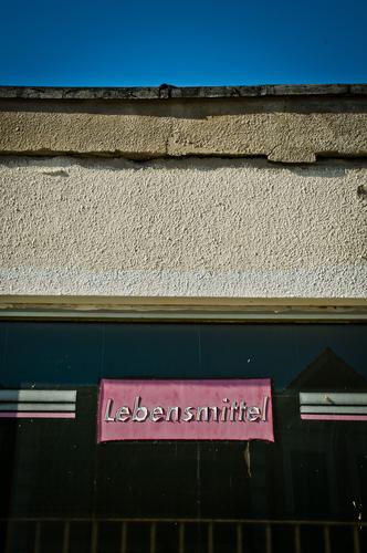 mindestens haltbar bis: Lebensmittel Gebäude Kaufhaus Mauer Wand Fenster Schaufenster Putz Schriftzeichen Typographie Beschriftung kaputt trashig blau rosa